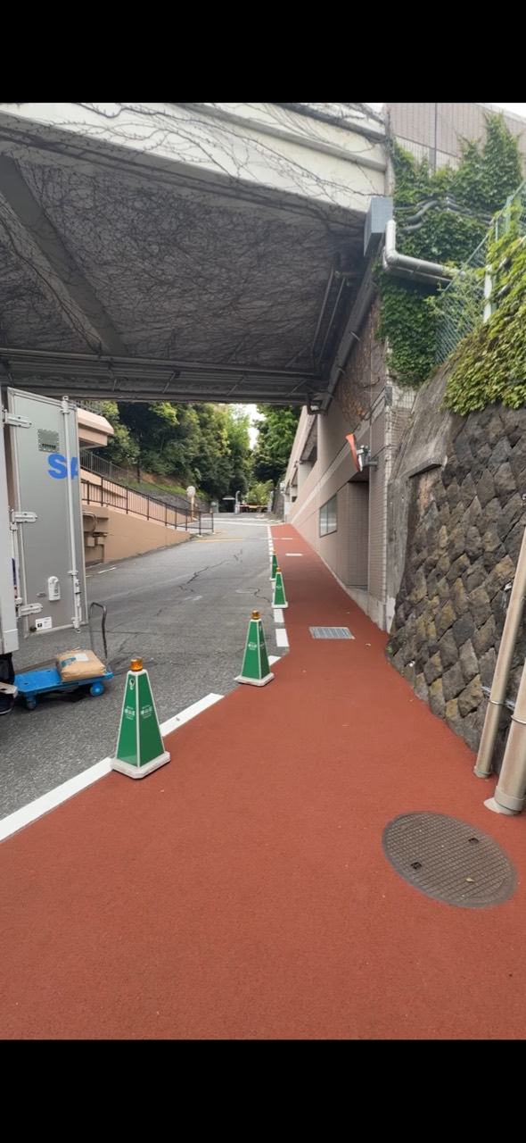 建物の下を通る敷地内の道。右側の赤い歩行スペースが白線と緑のコーンで車道から区切られている